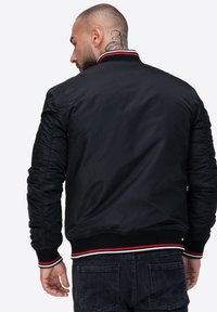 Czarna kurtka bombowiec z prążkowanym kołnierzem, z akcentami w czerwono-białe paski, o gładkiej, błyszczącej fakturze i dopasowanych mankietach.