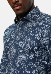 Marineblaue Hemd mit einem weißen Paisleymuster, mit Knöpfen und einem Haifischkragen. Hergestellt aus glattem Stoff mit einem leicht glänzenden Finish.