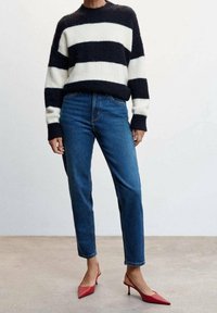 Pull en tricot rayé noir et blanc, jean bleu et escarpins rouges à bout pointu. Présente un col rond ainsi que des poignets et un ourlet côtelés.