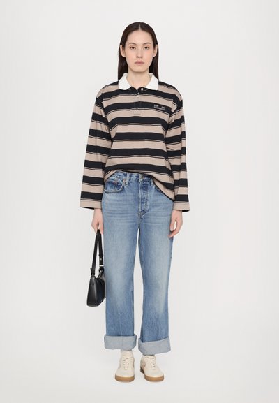 Langermet stripete polo-skjorte i beige og marineblå, kombinert med lyseblå jeans med oppbrett og kremfargede joggesko, holder en liten svart veske.