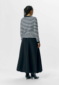 Chemise rayée à manches longues noire et blanche avec un col rond, associée à une jupe maxi noire fluide et des bottines noires.