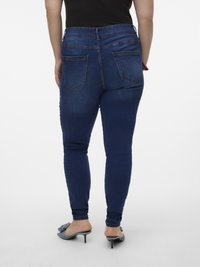 Dark blue skinny jeans with a high waist, featuring back pockets and a slightly faded texture, paired with low-heeled shoes.