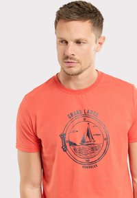 T-shirt col rond corail en coton doux, présentant un graphisme bleu marine représentant un voilier dans un cadre rond avec le texte "GRAND LARGE ARMORLUX."
