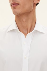 Vit skjorta med knappar fram och klassisk krage, med mjuk textur och minimal sömnadsdetalj, designad för en figurnära passform.