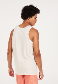 Lichtbeige tanktop met een losse pasvorm, met een subtiele textuur. Draagt met koraalkleurige short met kleine witte palmbomen.