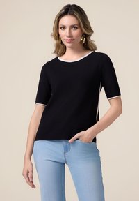 Top negru cu mânecă scurtă, cu decolteu rotund �și margine albă, textură netedă și laterale fâșii. Asortat cu blugi albaștri deschiși.