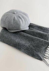Szara wełniana czapka z zaokrąglonym wierzchem i przeszytymi panelami, w połączeniu z ciemnoszarym szalem o miękkiej teksturze i frędzlami.