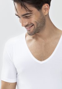 T-shirt V-neck en coton blanc avec des manches courtes et une texture lisse, dotée d'un décolleté profond et de détails de design minimalistes.