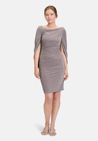 Robe argentée scintillante, longueur genou, avec un corsage ajusté, décolleté off-shoulder et manches cape fluides, associée à des sandales argentées à lanières.