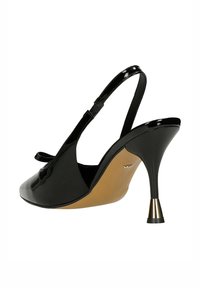 Czarny lakierowany but typu slingback z wąskim noskiem, beżową wkładką i szpilką z metalicznym złotym akcentem.