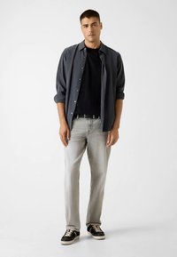 Graues freizeitliches Hemd über einem schwarzen T-Shirt, kombiniert mit hellgrauen Jeans und schwarzen Sneakers mit weißen Akzenten. Einfaches, modernes Design.