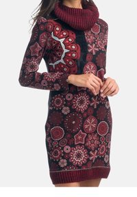 Robe en maille avec col bénitier, présentant un mélange de motifs floraux et géométriques en rouge, noir et blanc. Poignets et ourlet côtelés ajoutent de la texture.