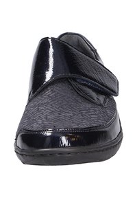 Scarpa nera slip-on con tomaia in tessuto texture e dettagli in pelle verniciata. Presenta una ampia fascia in Velcro per una facile regolazione e comfort.