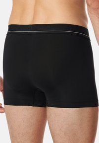 Schwarze Boxershorts aus glattem, dehnbarem Stoff mit einer engen Passform. Mit einem Bund, der ein dezentes weißes Akzent hat.