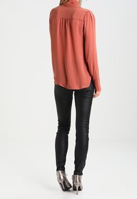 Mouwen lange, roestkleurige blouse met gathered achterkant detail, gedragen met strakke zwarte faux leren broek en zilveren haklaarzen.