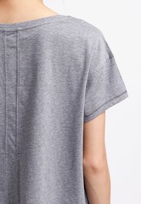 Szara bawełniana koszulka z luźnym krojem, krótkimi rękawami, zaokrąglonym dekoltem i widocznymi przeszyciami wzdłuż tylnego szwu.