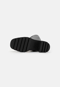 Černá gumová podrážka boty s horizontálními drážkami a rýhami; kulatá špička a plochý podpatek. Minimalistický design bez viditelných log nebo akcentů.