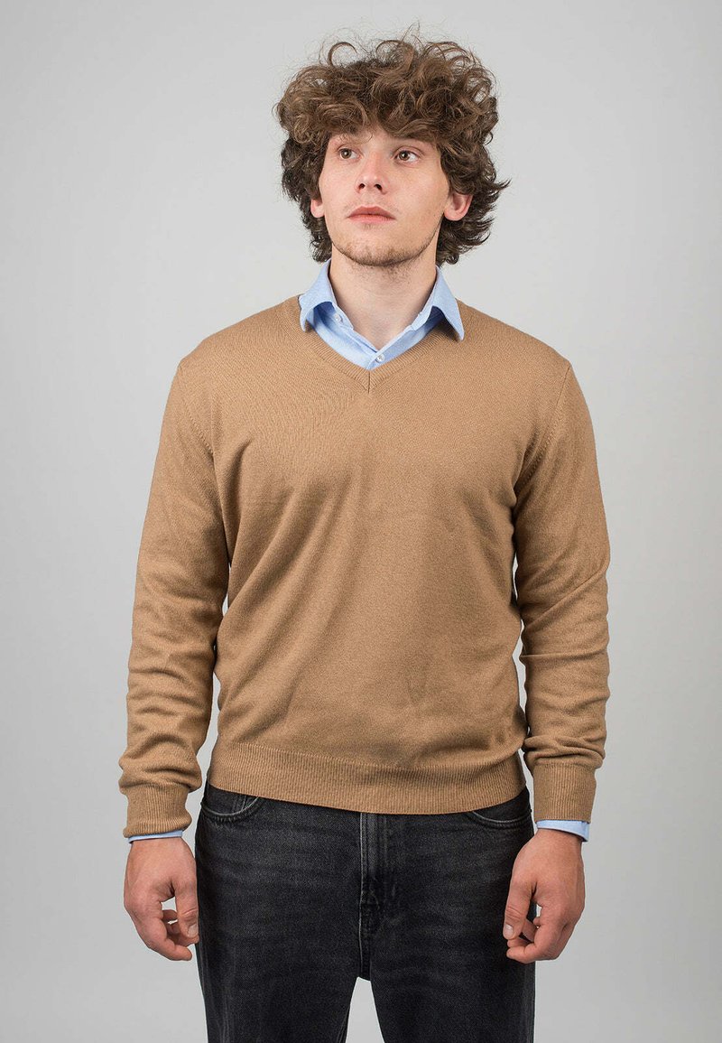 Valkoinen V-kaulusneule, joka on valmistettu pehmeästä neuloksesta, päällä vaaleansininen kauluspaita. Neuleessa on ribbireunat hihoissa ja helmassa.