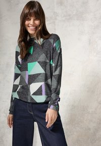 Grijze langearmige top met geometrische patronen in groen, teal, paars en wit. Gecombineerd met donkerdenim wijde broek.