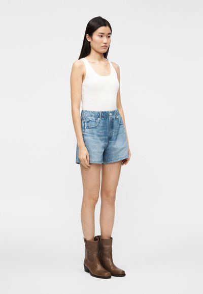 Débardeur blanc côtelé, short en jean bleu clair avec taille élastique, et bottines en cuir marron à talon bas.