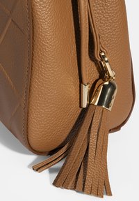 Camelkleurige leren handtas met een gevlochten band, gouden hardware en een kwastaccent aan de zijkant. Vierkante vorm met gestikte details.