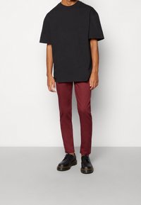 T-shirt oversize in cotone nero, pantaloni slim-fit bordeaux e scarpe nere. Design semplice, maniche corte, con una texture liscia e una leggera lucentezza.
