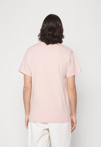 Ljusrosa t-shirt med kort ärm, rundad hals, gjord av mjukt tyg. Synliga sömmar på axlarna, avslappnad passform, utan mönster eller grafik.