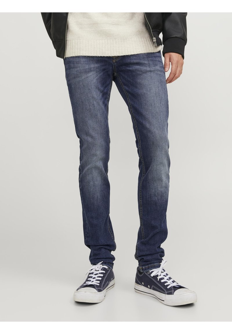 Jeans de mezclilla azul de corte recto, con una textura desgastada y sutiles detalles de costura, combinados con zapatillas de lona azul marino.