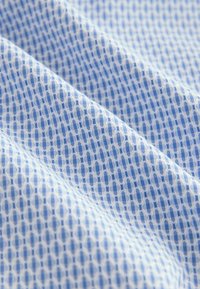 Tessuto blu chiaro a motivo geometrico, con piccoli diamanti e ovaliin una trama ripetuta su uno sfondo bianco.