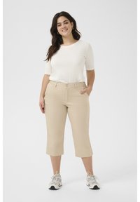 Beige cropped pants paired with a white short-sleeve top. The pants have a smooth texture and a classic button closure. Sneakers complete the look.