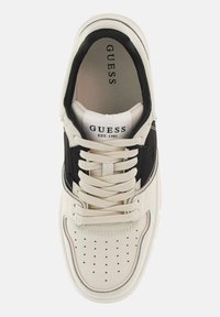 Sneaker bianca e nera con punta perforata, lacci spessi e linguetta imbottita. Presenta il marchio "GUESS" sulla linguetta e sul lato.