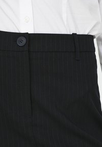 Zwarte gestreepte broek met een platte voorkant, voorzien van een enkele knoopsluiting, riemlussen en een gladde stofstructuur.