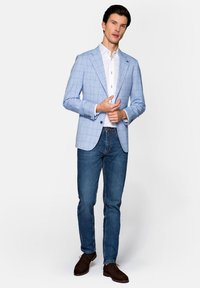 Jasnoniebieska marynarka w kratę na białej koszuli, w zestawieniu z ciemnymi dżinsami i brązowymi butami. Marynarka ma dopasowany krój i klapy o wycięciu.