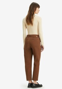 Brown cotton pants with a straight fit, featuring two back pockets and a high waist, paired with a beige ribbed long-sleeve top.