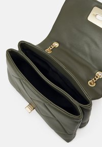 Zelenohnědá kabelka z umělé kůže s prošívaným designem, se zlatým uzávěrem a řetízkovým kováním. Uvnitř má dva oddíly s černým podšíváním.