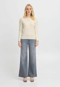 Maglione a maglia color crema con maniche lunghe, abbinato a jeans grigi chiari a gamba larga. Il maglione presenta un orlo a coste e un taglio rilassato.