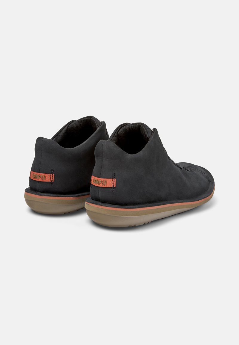 Bottines noires affichées de dos, montrant une texture lisse et un logo orange sur le talon. La semelle a un design léger et flexible.