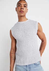 Grey sleeveless knit top with vertical ribbing texture, round neckline, and a relaxed fit. Worn with light blue denim jeans.