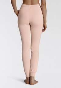Rosa Jogginghose aus weichem Baumwollmaterial, mit einem elastischen Bund, gerippten Säumen und einer glatten Textur, von hinten betrachtet.