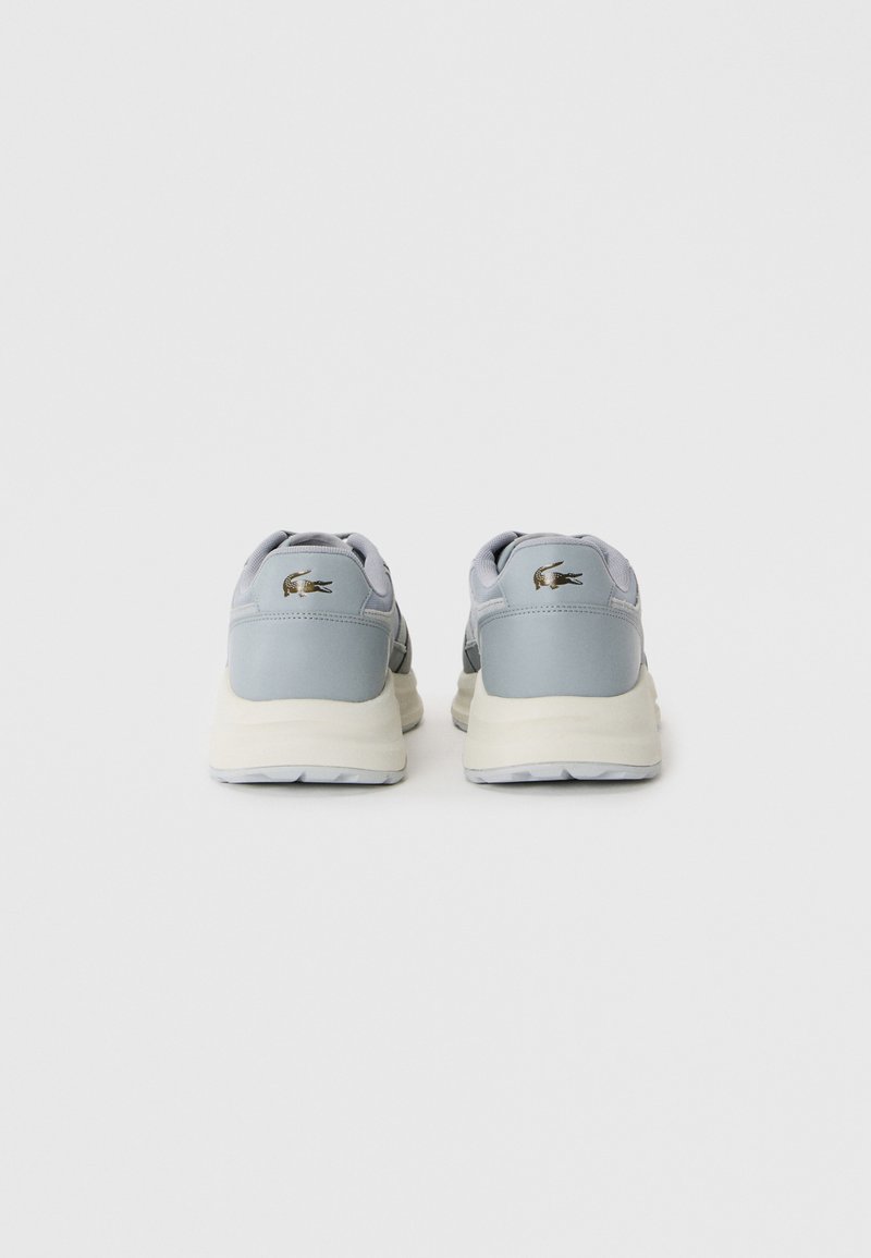 Une paire de baskets gris clair avec des semelles blanches, vue de l'arrière, comportant un petit logo d'animal sombre au niveau du talon.