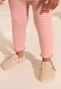 Chaussures en daim beige avec une bride et une boucle argentée, associées à des leggings rayés rose et blanc avec un ourlet festonné.