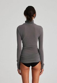 Maglione grigio a maniche lunghe con collo a imbuto, dal design aderente, morbido al tatto e con dettagli arricciati in vita, abbinato a pantaloni corti neri.