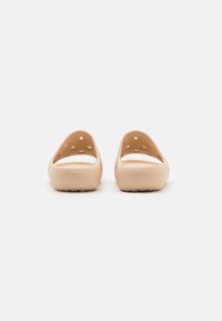 Beige Crocs klompen met open hiel, ronde ventilatiegaten aan de zijkanten, getextureerde zolen en een gladde afwerking. Herkenbaar merklogo aan de achterkant.