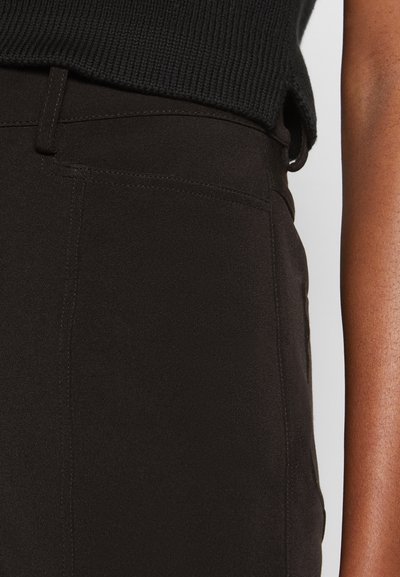Calças pretas de cintura alta com uma textura suave, costura detalhada e bolsos laterais, apresentadas ao lado de uma blusa de malha escura e canelada.
