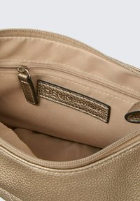 Interno della borsa texture oro, con una fodera liscia e tasca con zip. Include un'etichetta brandizzata in pelle.