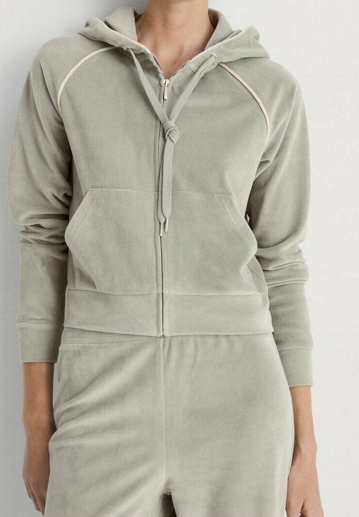 Sweat à capuche zippé gris clair avec cordon, poche kangourou et pantalon assorti porté par une personne debout sur un fond uni.