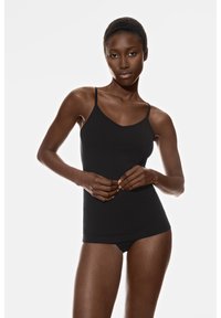 Zwarte cami met dunne bandjes, een gladde textuur en een aansluitend ontwerp. Het model draagt een bijpassende zwarte slip en staat tegen een witte achtergrond.