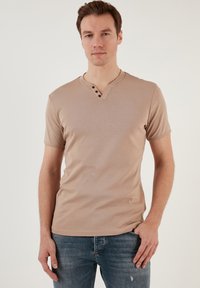 Beige košile s krátkým rukávem a výstřihem do V, s zapínáním na tři knoflíky. Vyrobena z hladkého materiálu, má jednoduchý design, přiléhavý střih a minimální detaily.