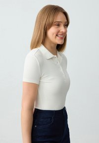 Witte geribde polo shirt met een kraag, korte mouwen en knoopdetail, gecombineerd met donkerblauwe high-waisted broek. Eenvoudig, passend ontwerp.