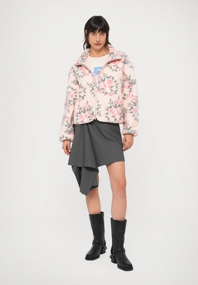 Fleecová bunda s ružovým kvetinovým vzorom, sivými akcentmi a celým zipsom. Dopĺňa ju sivá asymetrická sukňa a čierne čižmy po kolená.